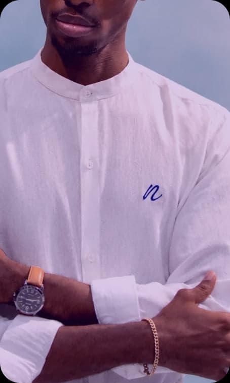 Man in a white linen shirt with an embroidered blue n, arms crossed