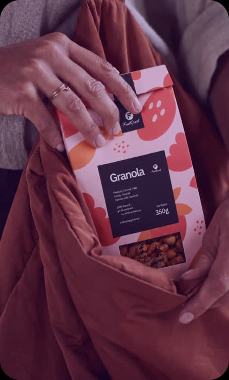 Hands tucking a Fruitvent granola box into a rust-coloured bag